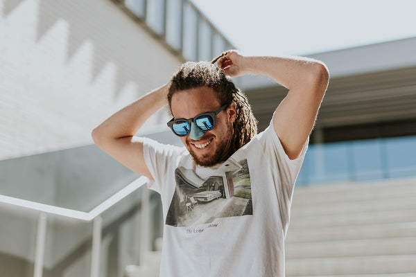 A smiling young man wears sunglasses and blue, reef safe Nöz sunscreen. 